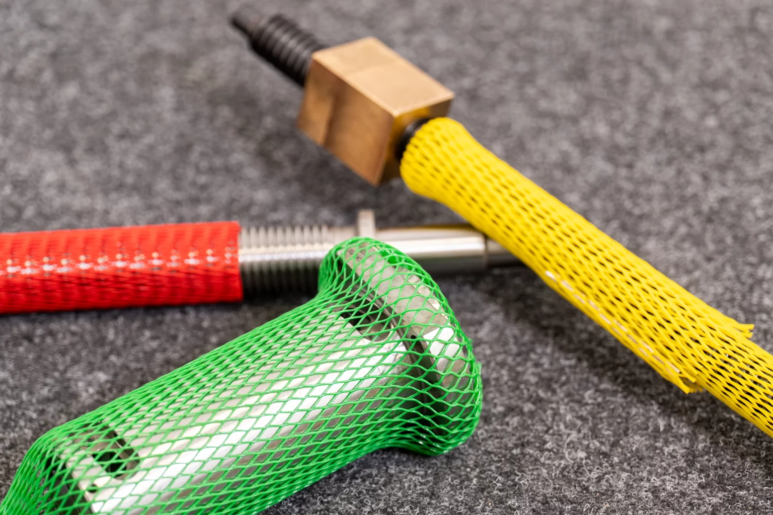 Metallteile mit farbigen Oberflächen-Schutznetzen in Grün, Rot und Gelb.