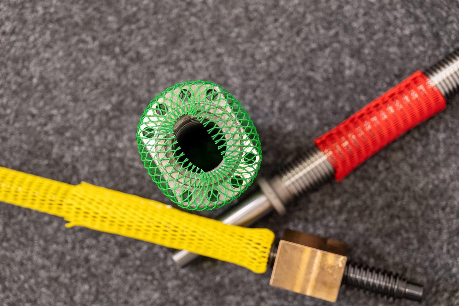 Metallteile mit farbigen Oberflächen-Schutznetzen in Grün, Rot und Gelb.